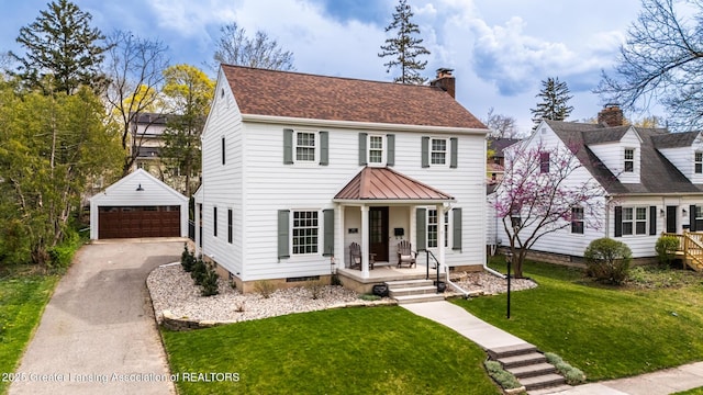 colonial house featuring a chimney, a standing seam roof, an outbuilding, a porch, and a garage