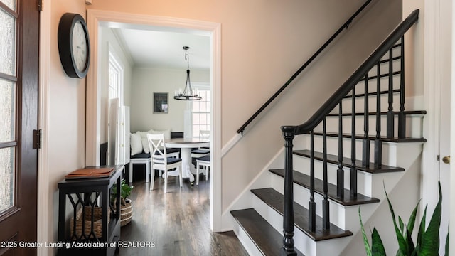 stairway with crown molding, an inviting chandelier, and wood finished floors