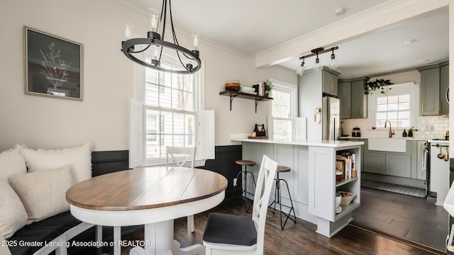dining area featuring dark wood-style flooring, ornamental molding, a wainscoted wall, and a notable chandelier