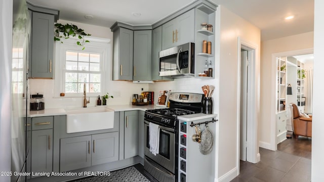 kitchen featuring decorative backsplash, open shelves, a sink, appliances with stainless steel finishes, and gray cabinetry