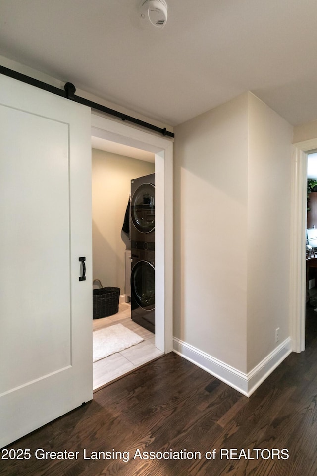 hall with wood finished floors, a barn door, stacked washer / dryer, and baseboards