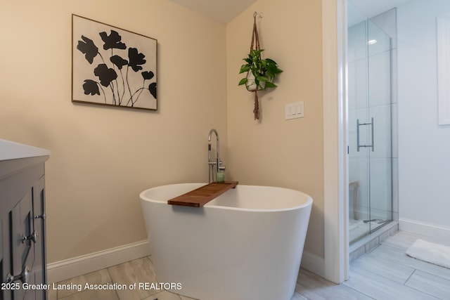 full bathroom with a freestanding bath, a shower stall, vanity, and baseboards