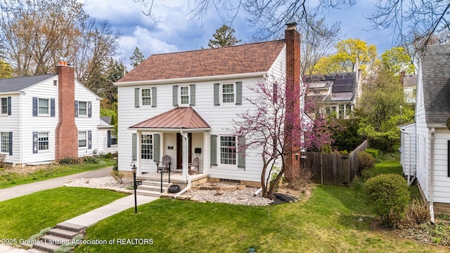 view of front of house with a chimney, roof with shingles, a front yard, fence, and a porch