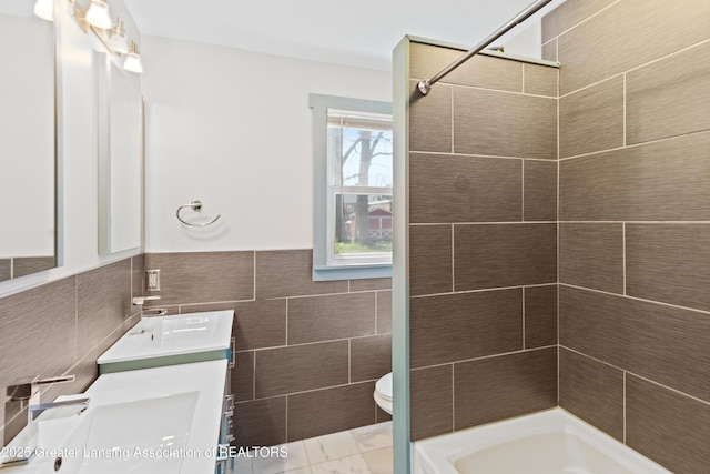 bathroom with a sink, double vanity, toilet, tile walls, and a shower