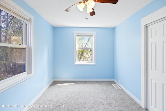 spare room with carpet floors, baseboards, a ceiling fan, and visible vents