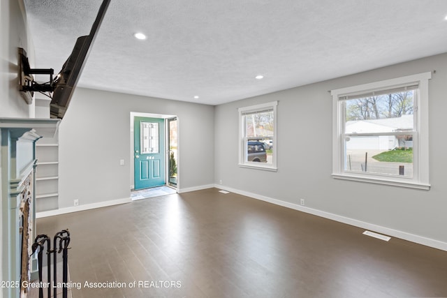unfurnished living room with a textured ceiling, recessed lighting, baseboards, visible vents, and dark wood-style floors