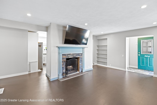 unfurnished living room featuring dark wood-style flooring, a fireplace with raised hearth, built in shelves, recessed lighting, and baseboards