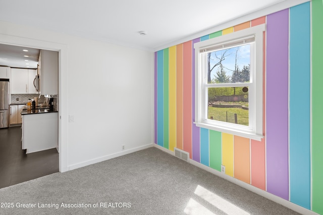 spare room featuring baseboards, wallpapered walls, visible vents, and dark carpet