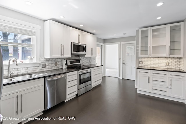 kitchen with a sink, backsplash, dark countertops, and stainless steel appliances