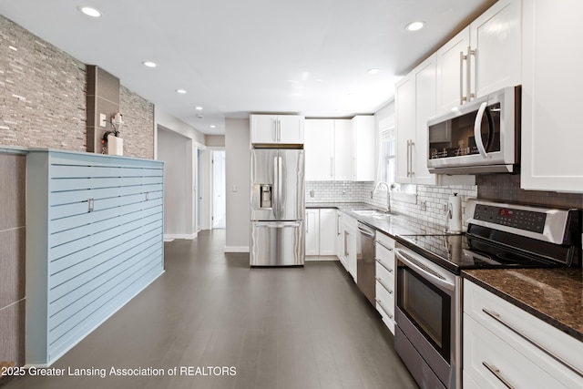 kitchen featuring appliances with stainless steel finishes, a sink, dark stone countertops, white cabinetry, and tasteful backsplash