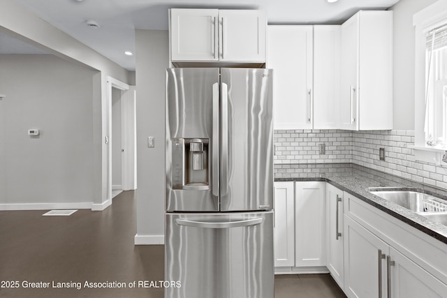 kitchen with stainless steel fridge, dark stone counters, and white cabinets