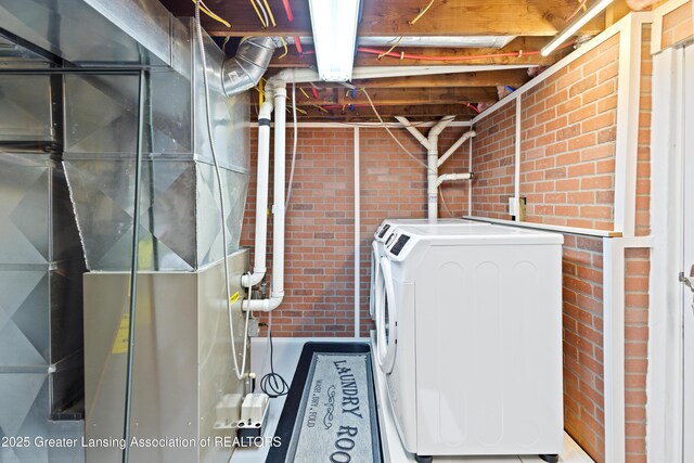 laundry area with heating unit, separate washer and dryer, laundry area, and brick wall