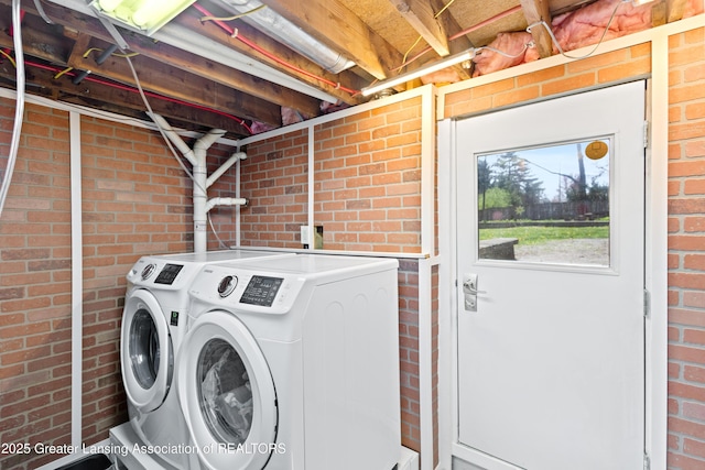 laundry area featuring brick wall, washing machine and dryer, and laundry area