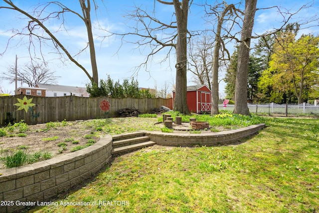 view of yard featuring a storage unit, a fenced backyard, a fire pit, and an outbuilding