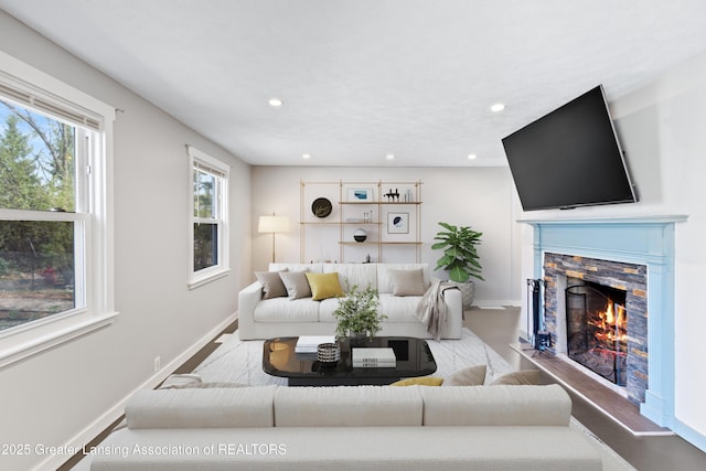 living room with baseboards, recessed lighting, a stone fireplace, and wood finished floors