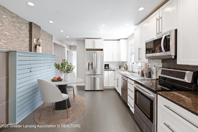 kitchen with appliances with stainless steel finishes, a sink, dark stone counters, white cabinetry, and backsplash