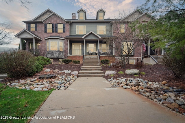 view of front of home with brick siding, a porch, and stairs