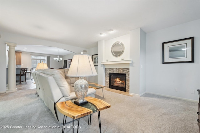 living area featuring a notable chandelier, decorative columns, a stone fireplace, baseboards, and light colored carpet