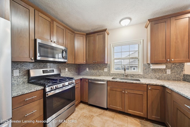 kitchen with appliances with stainless steel finishes, light stone counters, backsplash, and a sink