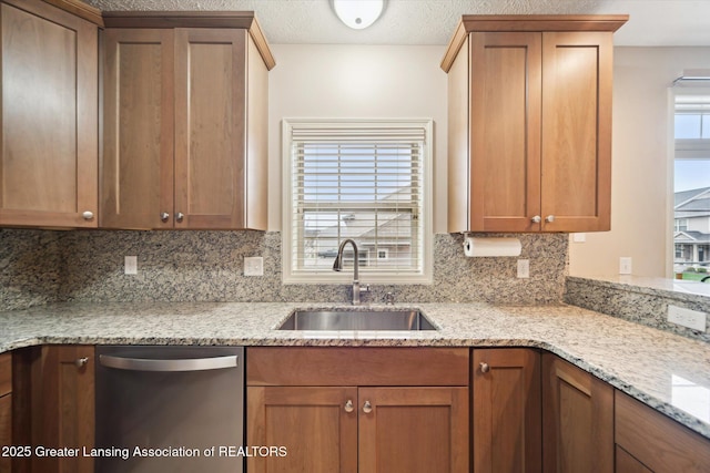 kitchen with light stone counters, brown cabinets, tasteful backsplash, a sink, and dishwasher