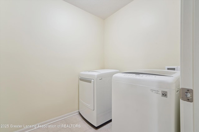 clothes washing area featuring light tile patterned floors, washing machine and clothes dryer, laundry area, and baseboards