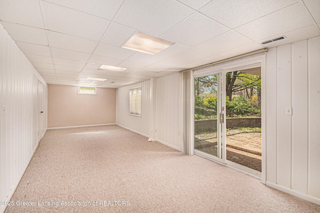 carpeted spare room featuring visible vents, wood walls, a paneled ceiling, and baseboards