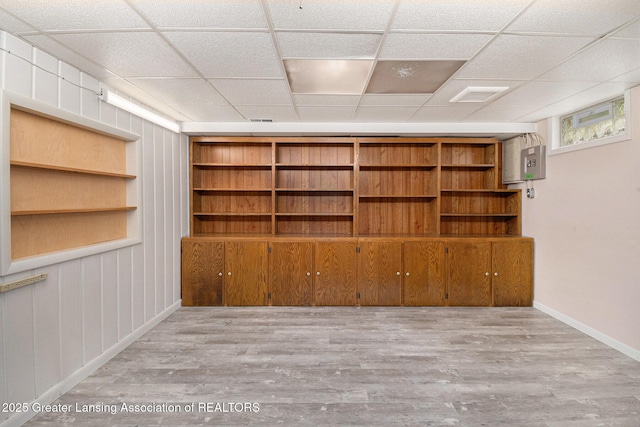 finished below grade area with a paneled ceiling, baseboards, and wood finished floors