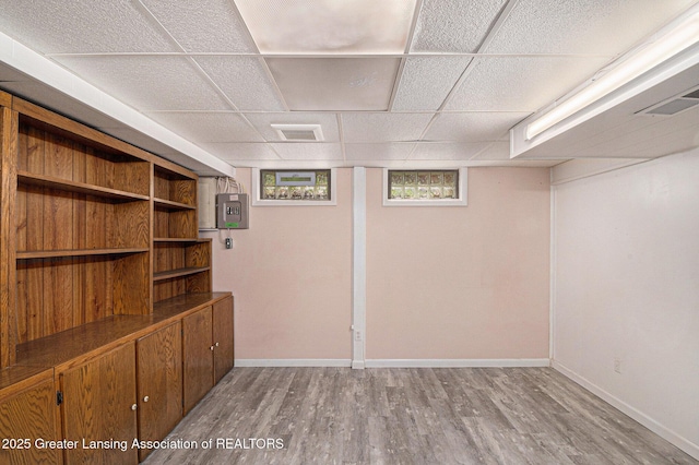 basement with electric panel, visible vents, wood finished floors, baseboards, and a drop ceiling