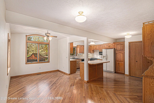 kitchen with light countertops, a textured ceiling, brown cabinets, and white refrigerator with ice dispenser