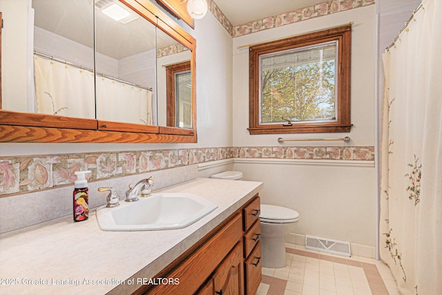 bathroom featuring visible vents, vanity, toilet, baseboards, and a wainscoted wall
