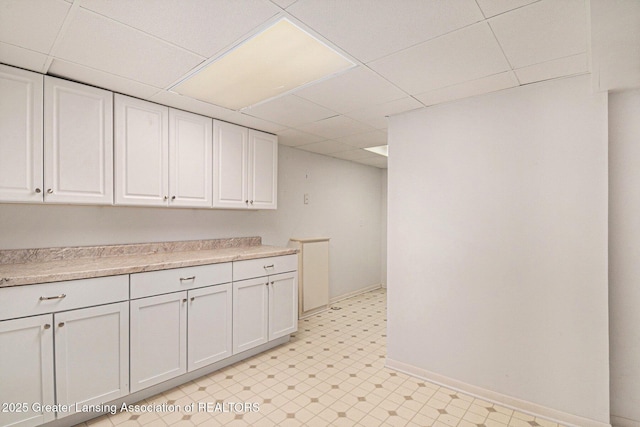 interior space featuring a paneled ceiling, light countertops, baseboards, light floors, and white cabinetry