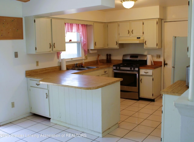 kitchen featuring a sink, freestanding refrigerator, a peninsula, stainless steel range with gas cooktop, and under cabinet range hood