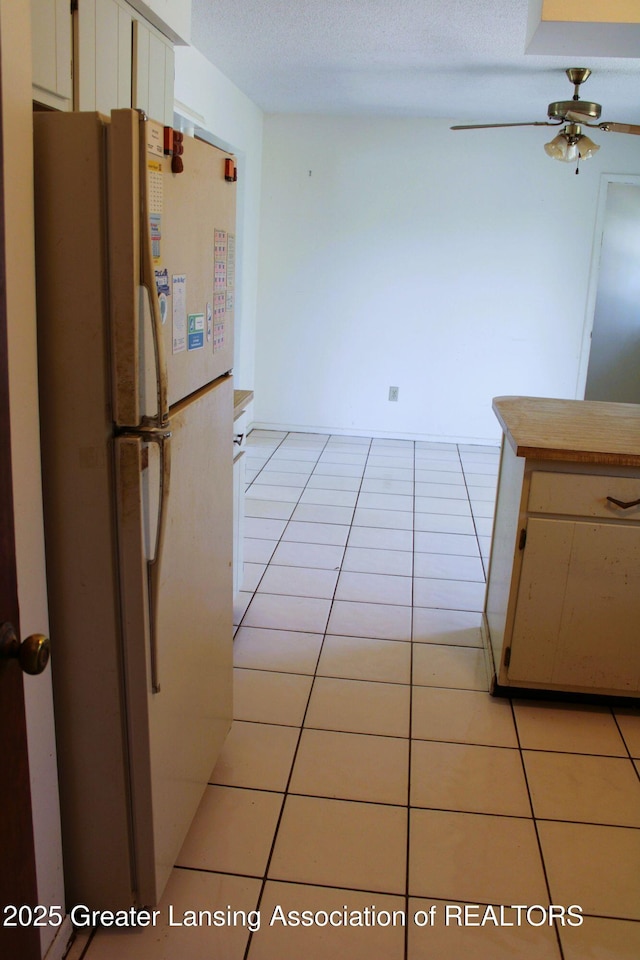 kitchen featuring light tile patterned floors, white cabinets, freestanding refrigerator, and ceiling fan
