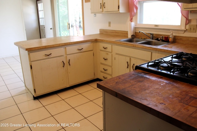 kitchen with butcher block countertops, a sink, a peninsula, and light tile patterned floors