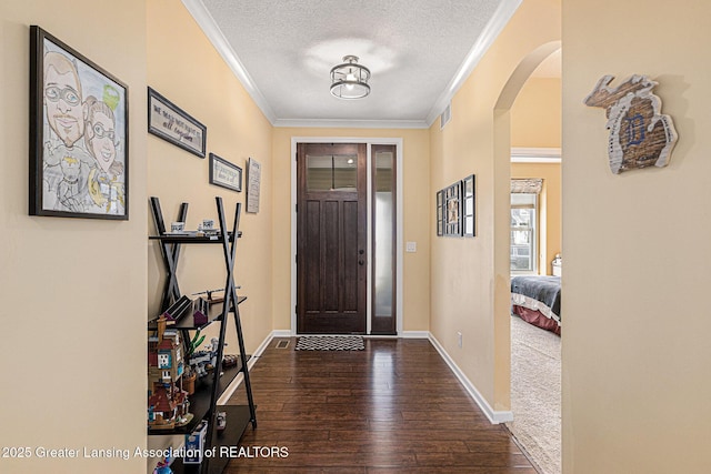 foyer entrance featuring a textured ceiling, baseboards, ornamental molding, arched walkways, and hardwood / wood-style flooring