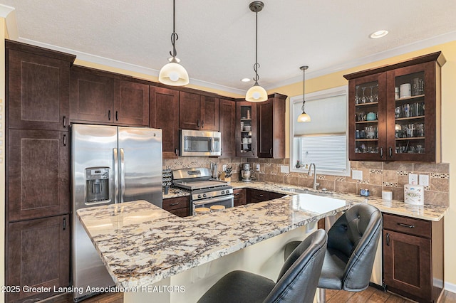 kitchen featuring dark brown cabinetry, light stone counters, a breakfast bar, appliances with stainless steel finishes, and a sink