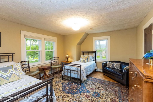 620 Ardson Rd, East Lansing, MI 48823 - bedroom featuring multiple windows, wood finished floors, a textured ceiling, and a baseboard heating unit