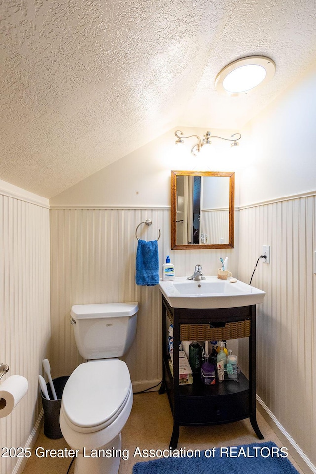 620 Ardson Rd, East Lansing, MI 48823 - bathroom with lofted ceiling, a textured ceiling, toilet, vanity, and a wainscoted wall
