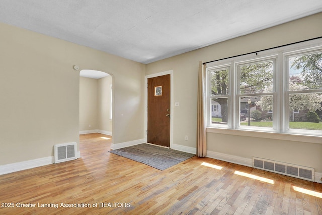 foyer entrance featuring arched walkways, light wood-style flooring, and baseboards