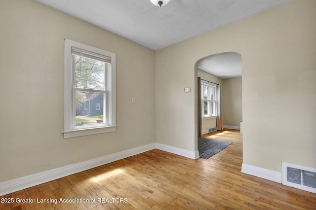 spare room featuring arched walkways, plenty of natural light, and light wood-style flooring