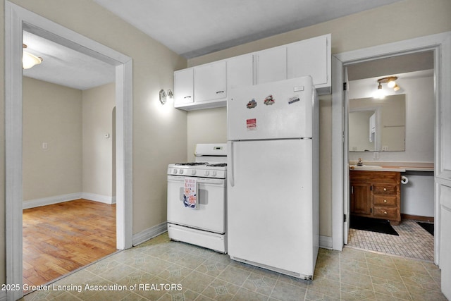 kitchen featuring white appliances, baseboards, white cabinets, light countertops, and a sink