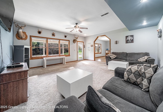 living area featuring carpet flooring, visible vents, baseboards, arched walkways, and a ceiling fan