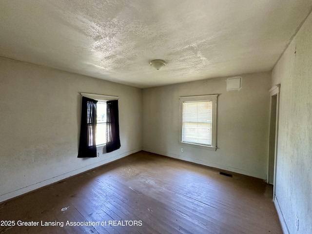 spare room with a textured ceiling, visible vents, a healthy amount of sunlight, and hardwood / wood-style floors