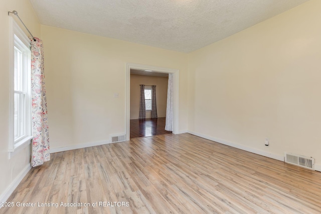 spare room featuring visible vents, a textured ceiling, baseboards, and light wood-type flooring