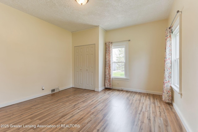unfurnished bedroom with a textured ceiling, visible vents, wood finished floors, and a closet