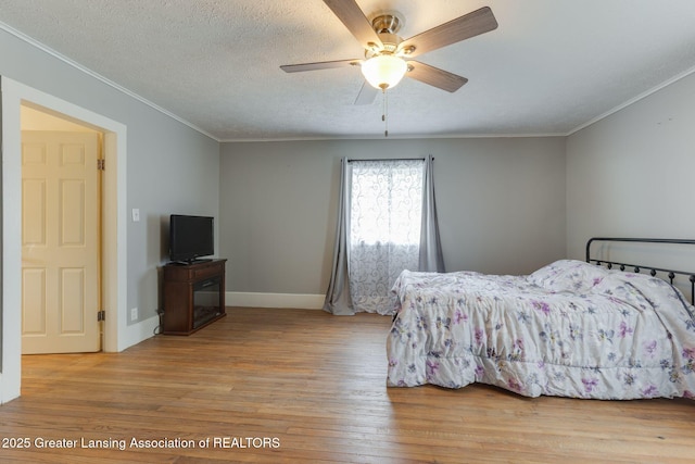 bedroom featuring a ceiling fan, baseboards, ornamental molding, and light wood-type flooring