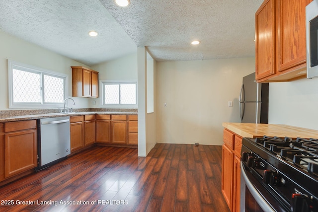 kitchen with appliances with stainless steel finishes, brown cabinetry, a textured ceiling, and dark wood-type flooring