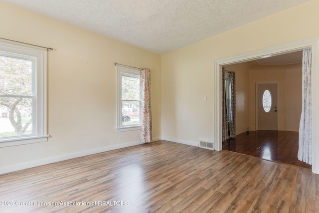 unfurnished room featuring baseboards, a textured ceiling, visible vents, and wood finished floors