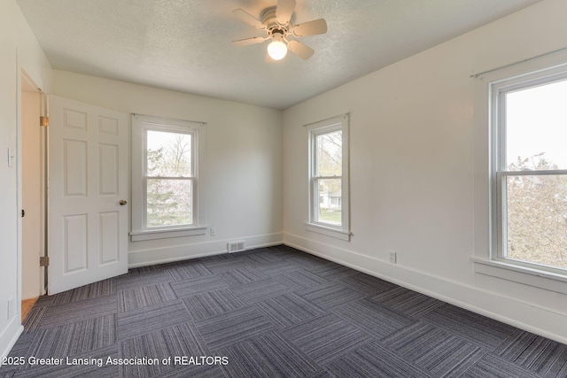 empty room featuring visible vents, dark colored carpet, baseboards, a textured ceiling, and a ceiling fan