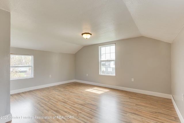 additional living space featuring a healthy amount of sunlight, baseboards, vaulted ceiling, and light wood finished floors